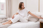 Woman in white lounge wear sitting on a bed in a bright room