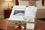 White Bedsheet, bathrobe and towels in a gift box with a ribbon on a wooden table.