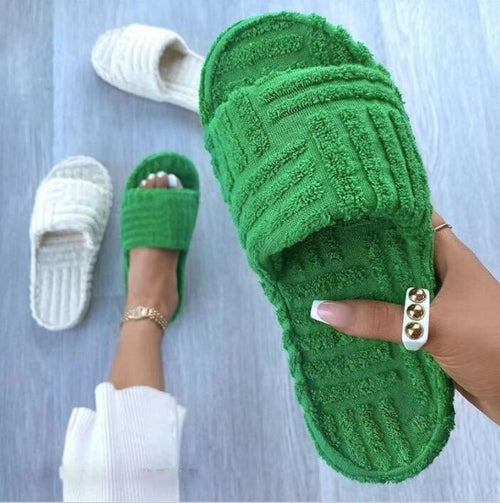 Green textured slippers held  on a light gray background