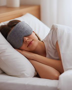 Person wearing a gray sleep mask lying on a bed.