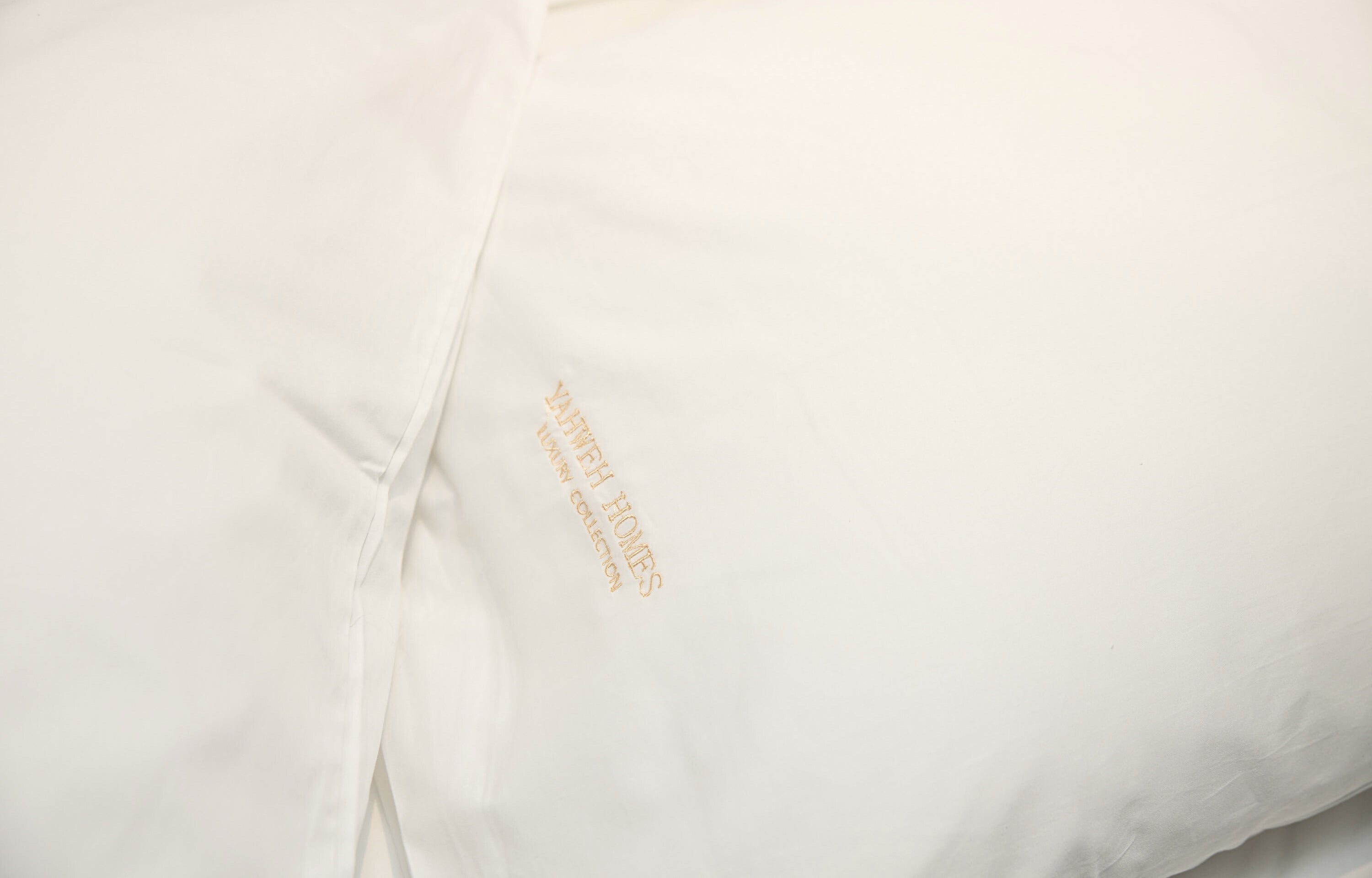 Close-up of a white pillow case with Yahweh Homes Embroidery.
