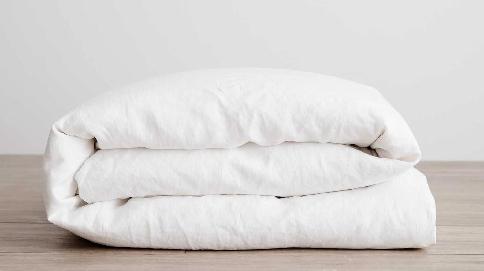 Folded white Duver Cover on a wooden surface with a light gray background