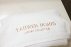 White face towel with 'Yahweh Homes Luxury Collection' embroidery on a light background