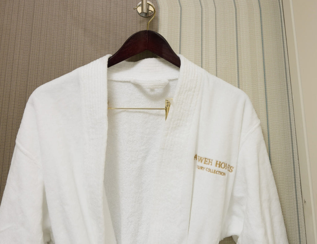 White robe with gold text on a wooden hanger against a neutral background