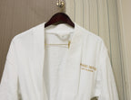White robe with gold text on a wooden hanger against a neutral background