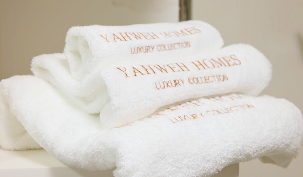 Stack of white towels with 'YAHWEH HOMES' branding.