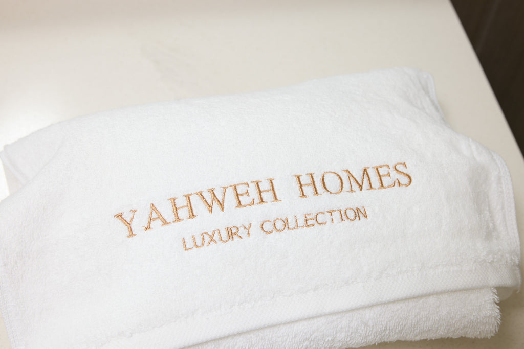 White towel with 'Yahweh Homes Luxury Collection' embroidery on a light background