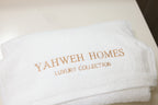 White towel with 'Yahweh Homes Luxury Collection' embroidery on a light background