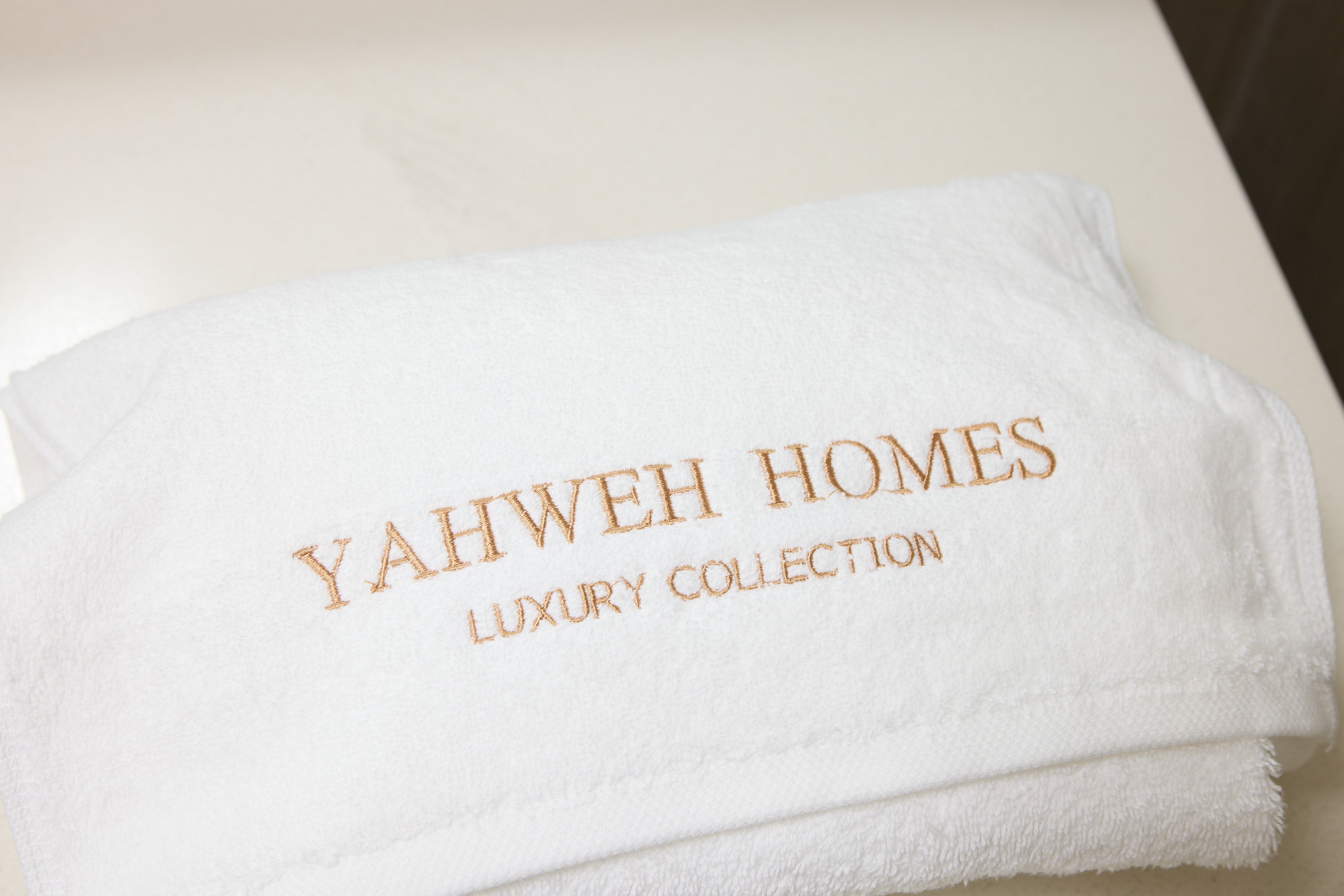 White towel with 'Yahweh Homes Luxury Collection' embroidery on a light background