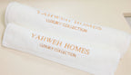 Two white towels with 'Yahweh Homes Luxury Collection' embroidery on a beige background
