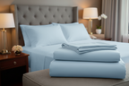 Light blue bedding set on a bed in a bedroom setting with lamps and decor.