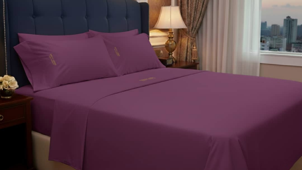 Purple bed sheets and pillows with YAHWEH HOMES LUXURY COLLECTION inscription on a bed in a bedroom 
